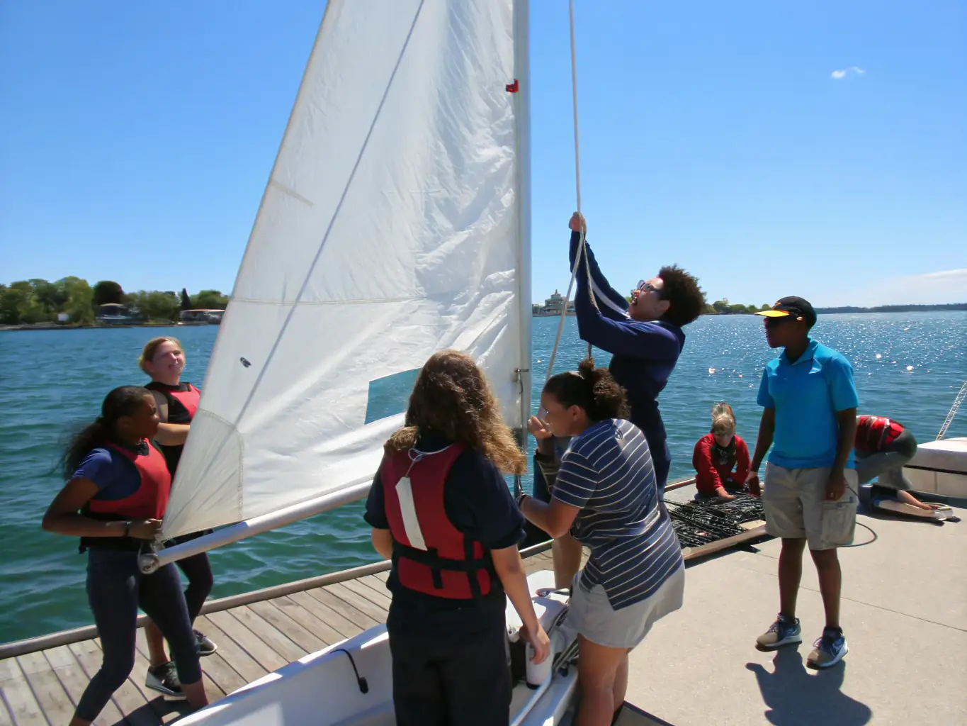 A group of diverse individuals participating in a sailing lesson on a sunny day, showcasing teamwork and skill-building.